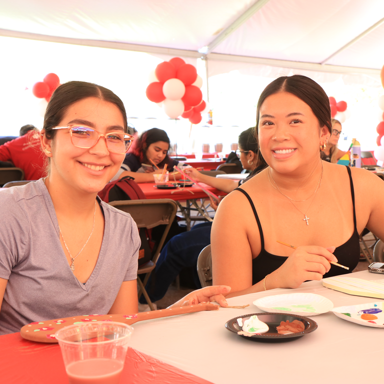 Two women smiling while painting small oars for Weeks of Welcome at IU Indianapolis.