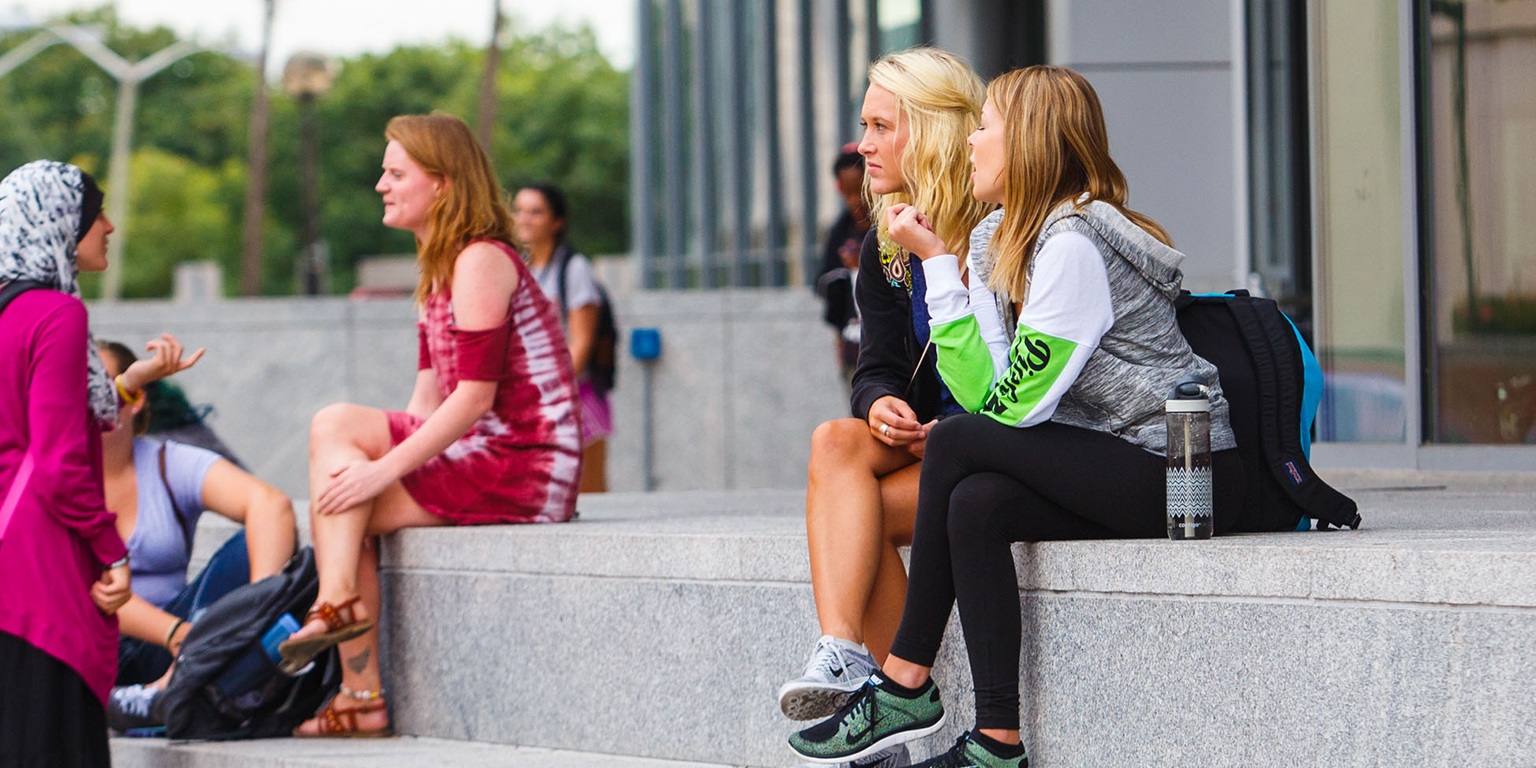 Two students sit outside of the campus center and talk.