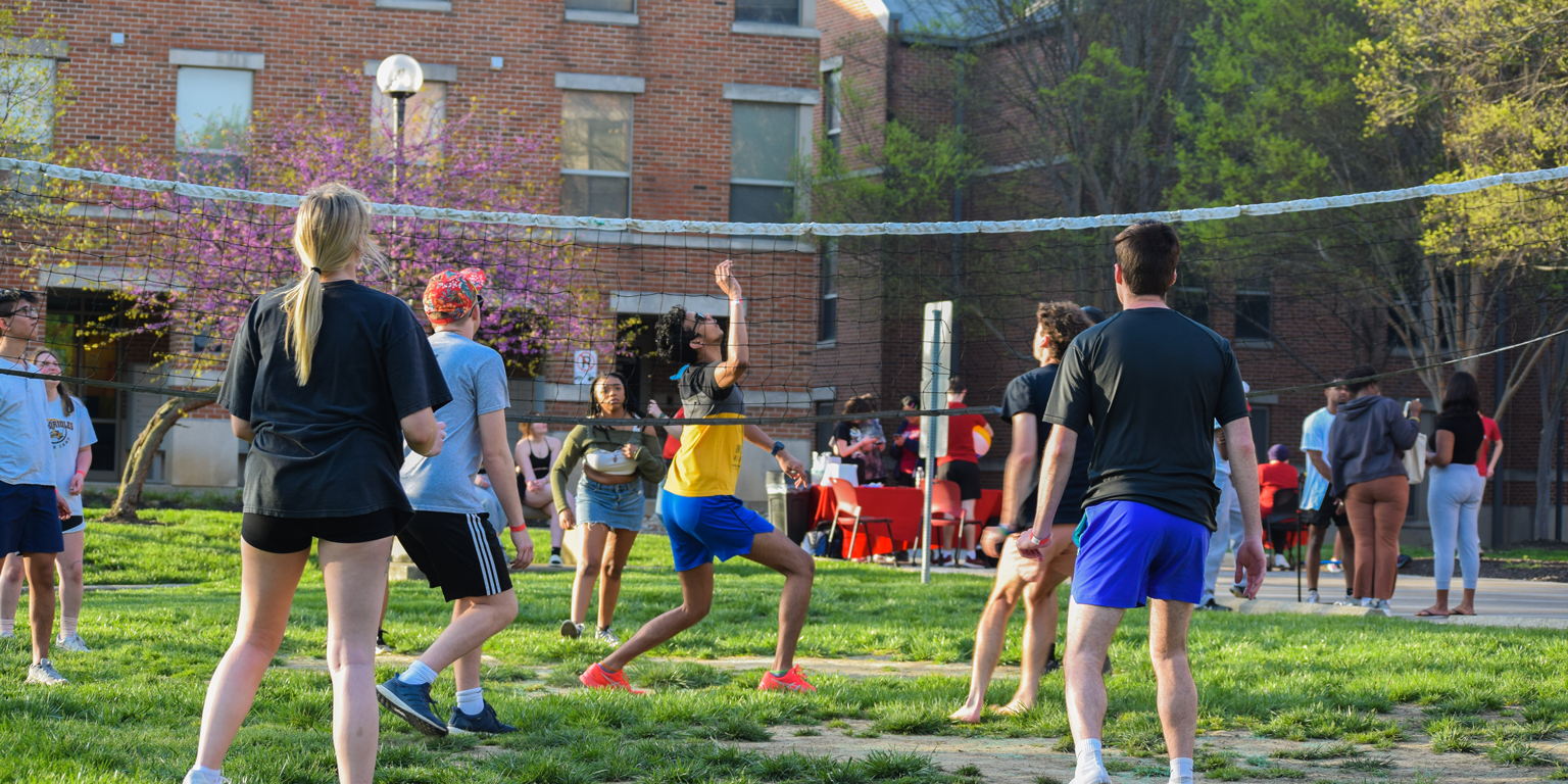 students playing volleyball outside of a dorm hall.